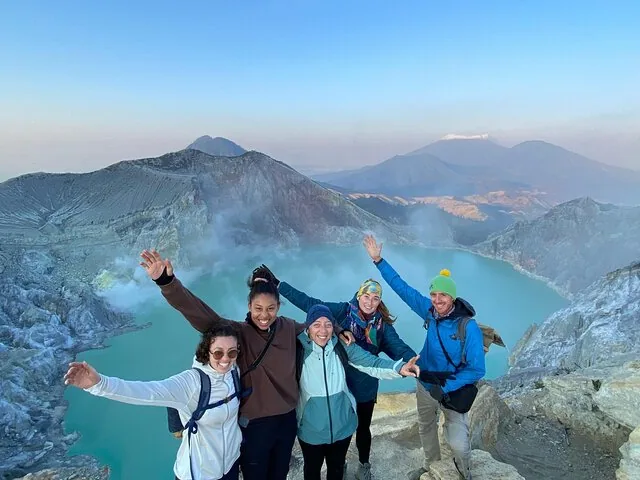 Group of friends cheering at the edge of a stunning turquoise crater lake.