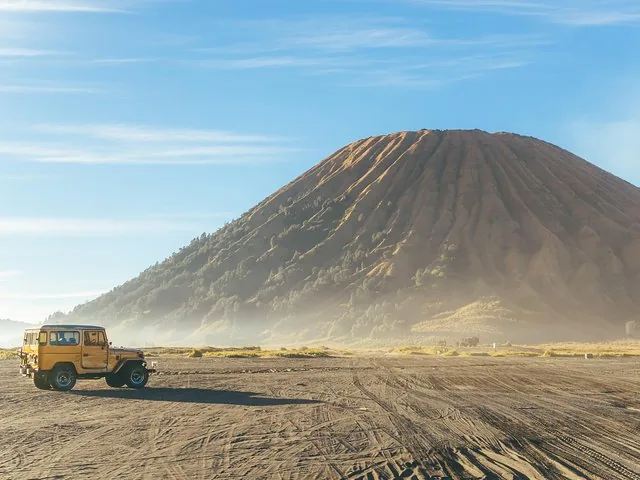 A yellow jeep parked on a dusty plain with Mount Bromo in the background.