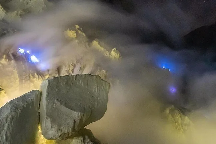 Mesmerizing blue flames burning on a rocky surface amidst sulfurous smoke.