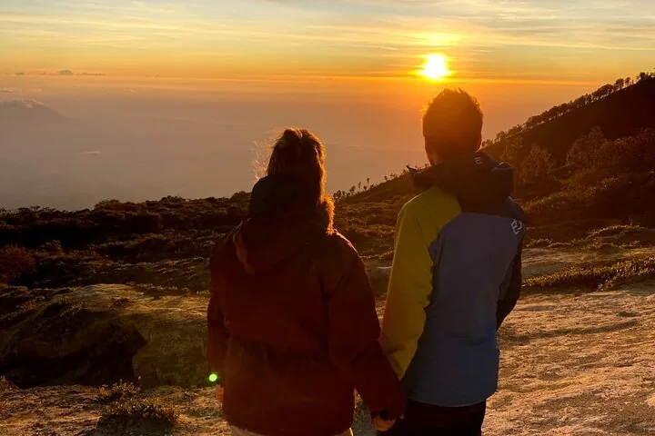 Couple holding hands and watching a magnificent sunrise from a high vantage point.